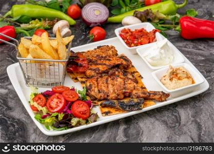 Grilled chicken thigh on white porcelain plate with french fries and salad