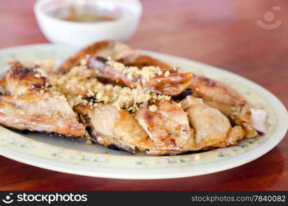 Grilled chicken with fried garlic on dish served with spicy sauce in bowl