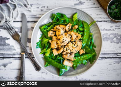 Grilled chicken with spinach,arugula and peas on rustic wooden background