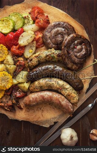 Grilled different meat and fish sausages with vegetables and spices on wooden background. Grilled sausages with vegetables
