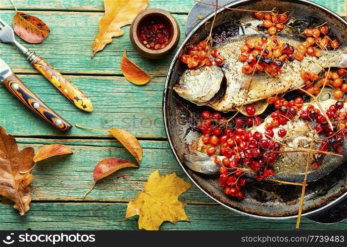 Grilled dorado with autumn berries in a pan. Fried fish with viburnum on wooden surface. Baked fish in viburnum syrup