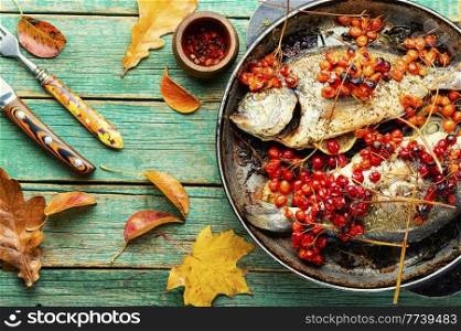 Grilled dorado with autumn berries in a pan. Fried fish with viburnum on wooden surface. Baked fish in viburnum syrup