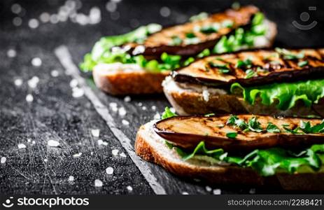 Grilled eggplant sandwich on a stone board. On a black background. High quality photo. Grilled eggplant sandwich on a stone board.