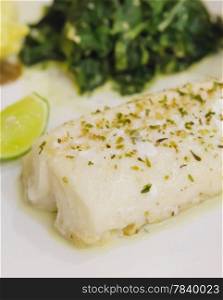 grilled fish. close up fillet fish steak with spinach and lime on white plate