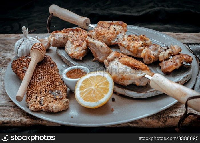Grilled lemon herb chicken thighs on metal skewers with Honey served on Ceramic plate. BBQ chicken skewers marinade ready to eat, Selective focus.