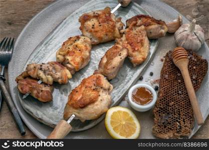 Grilled lemon herb chicken thighs on metal skewers with Honey served on Ceramic plate. BBQ chicken skewers marinade ready to eat, Selective focus.
