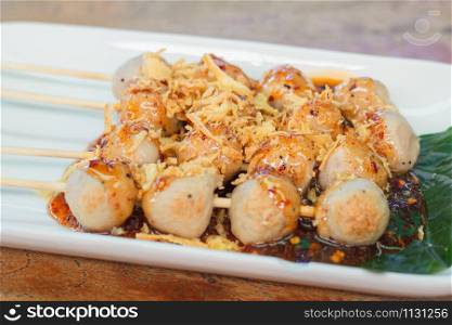 Grilled meat balls on sticks with spicy sauce on top with deep fried shallots.