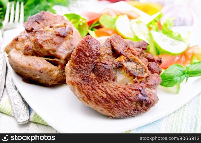 Grilled meat turkey in a white plate with slices of tomato, cucumber, sweet pepper and basil on the background light wooden boards
