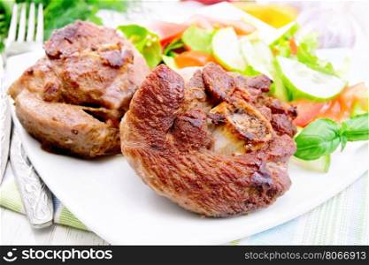Grilled meat turkey in a white plate with slices of tomato, cucumber, sweet pepper and basil on the background light wooden boards