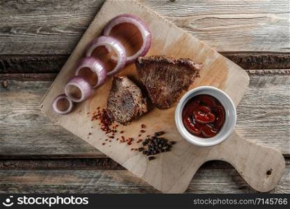 grilled meat with spices and tomato sauce on a worn wooden background