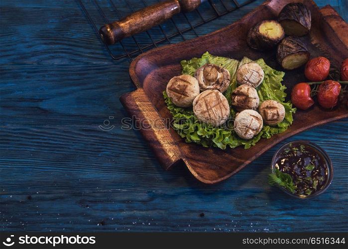 Grilled mushrooms champignons with vegetable on a blue wooden background. Grilled mushrooms champignons. Grilled mushrooms champignons
