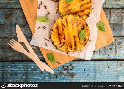Grilled pineapple slices on wooden table.