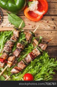 Grilled pork and chicken kebab with paprika in round wooden plate of lettuce salad, on wooden background with tomatoes and paprika.
