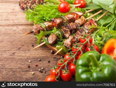 Grilled pork and chicken kebab with paprika in round wooden plate of lettuce salad, on wooden background with tomatoes and paprika.