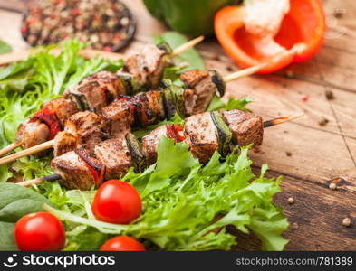 Grilled pork and chicken kebab with paprika in round wooden plate of lettuce salad, on wooden background with tomatoes and paprika.