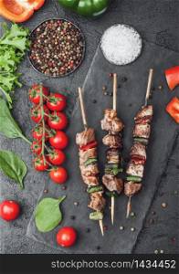 Grilled pork and chicken kebab with paprika on stone chopping board with salt, pepper and tomatoes on black background. Fresh lettuce and paprika pepper.