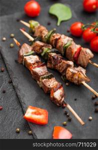 Grilled pork and chicken kebab with paprika on stone chopping board with salt, pepper and tomatoes on black. Macro