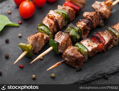 Grilled pork and chicken kebab with paprika on stone chopping board with salt, pepper and tomatoes on black. Macro