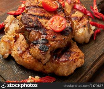 grilled pork pieces of meat on a grill lie on a vintage wooden board, close up
