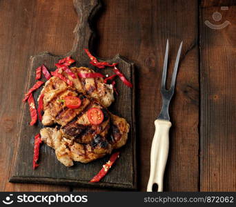 grilled pork pieces of meat on a grill lie on a vintage wooden board, close up