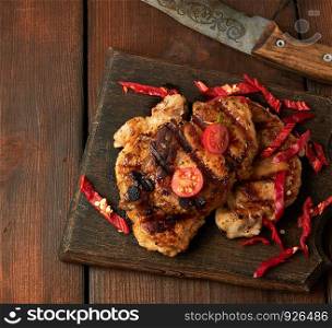 grilled pork pieces of meat on a grill lie on a vintage wooden board, close up