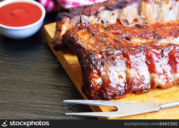 grilled pork ribs on a wooden cutting board with kitchen fork for meat and tomato ketchup. grilled pork ribs on a cutting board