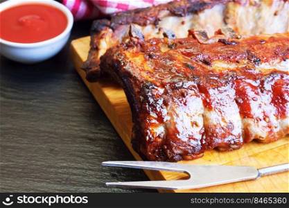 grilled pork ribs on a wooden cutting board with kitchen fork for meat and tomato ketchup. grilled pork ribs on a cutting board