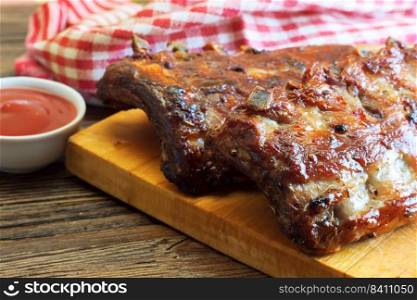 grilled pork ribs on a wooden cutting board with tomato ketchup on brown wooden surface.. grilled pork ribs on a cutting board
