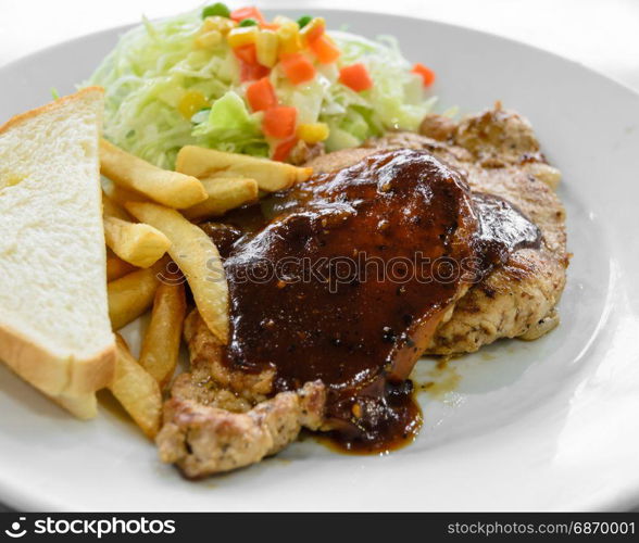 Grilled pork steak fillet with black pepper sauce, vegetable salad, bread and french fries on white plate