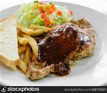 Grilled pork steak fillet with black pepper sauce, vegetable salad, bread and french fries on white plate