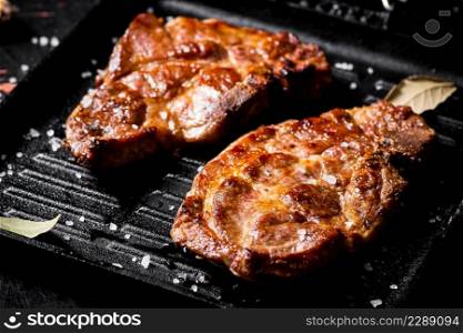 Grilled pork steak in a frying pan. Against a dark background. High quality photo. Grilled pork steak in a frying pan.