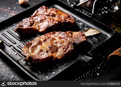 Grilled pork steak in a frying pan. Against a dark background. High quality photo. Grilled pork steak in a frying pan.