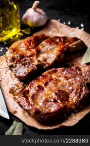 Grilled pork steak on paper on the table. On a black background. High quality photo. Grilled pork steak on paper on the table. 