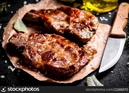 Grilled pork steak on paper on the table. On a black background. High quality photo. Grilled pork steak on paper on the table.