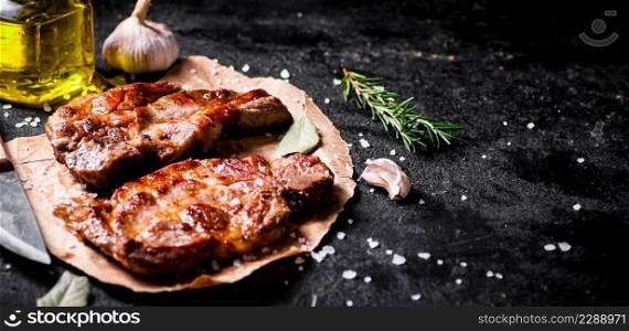 Grilled pork steak on paper on the table. On a black background. High quality photo. Grilled pork steak on paper on the table. 