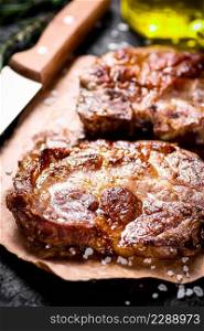 Grilled pork steak on paper on the table. On a black background. High quality photo. Grilled pork steak on paper on the table.