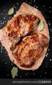 Grilled pork steak on paper with bay leaf. Against a dark background. High quality photo. Grilled pork steak on paper with bay leaf.