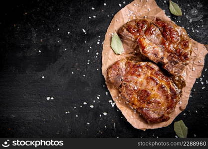 Grilled pork steak on paper with bay leaf. Against a dark background. High quality photo. Grilled pork steak on paper with bay leaf.