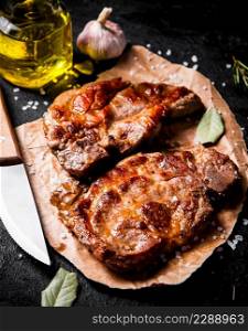 Grilled pork steak on paper with bay leaf. Against a dark background. High quality photo. Grilled pork steak on paper with bay leaf.