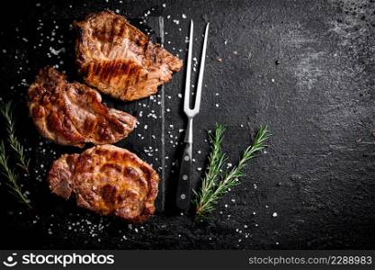 Grilled pork steak with a sprig of rosemary. On a black background. High quality photo. Grilled pork steak with a sprig of rosemary.