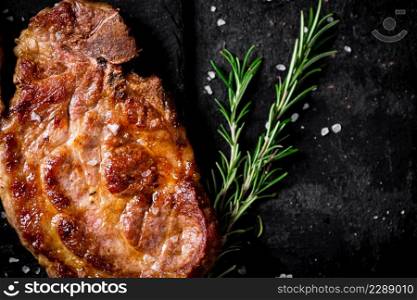 Grilled pork steak with a sprig of rosemary. On a black background. High quality photo. Grilled pork steak with a sprig of rosemary.