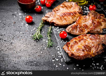 Grilled pork steak with cherry tomatoes and rosemary. On a black background. High quality photo. Grilled pork steak with cherry tomatoes and rosemary.