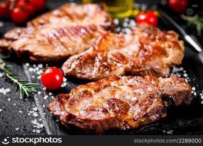 Grilled pork steak with cherry tomatoes and rosemary. On a black background. High quality photo. Grilled pork steak with cherry tomatoes and rosemary.