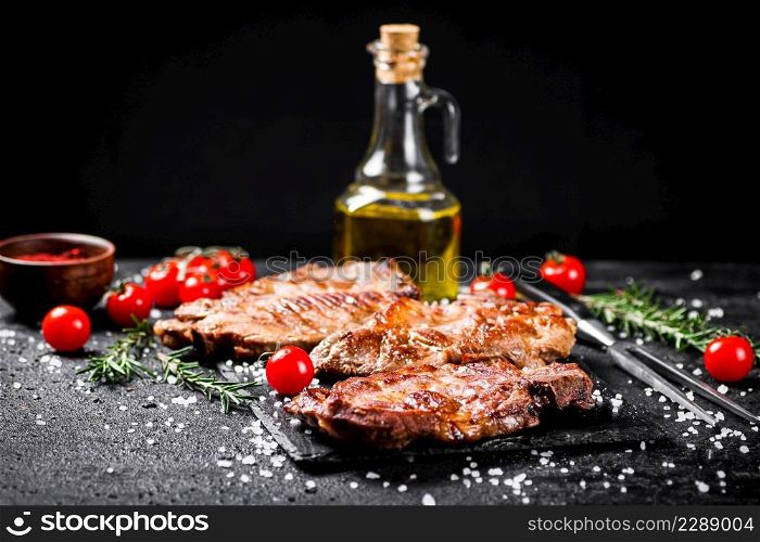 Grilled pork steak with cherry tomatoes and rosemary. On a black background. High quality photo. Grilled pork steak with cherry tomatoes and rosemary.