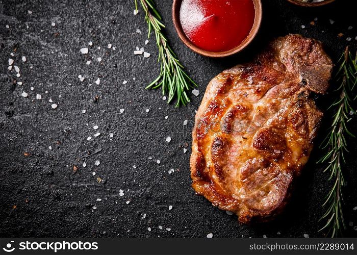 Grilled pork steak with tomato sauce and rosemary. On a black background. High quality photo. Grilled pork steak with tomato sauce and rosemary.