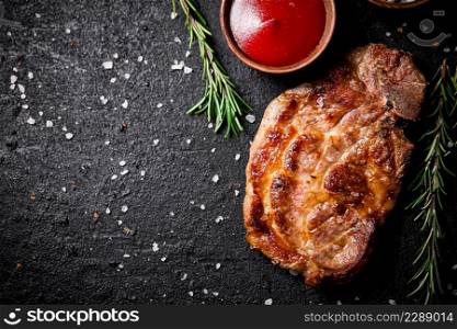 Grilled pork steak with tomato sauce and rosemary. On a black background. High quality photo. Grilled pork steak with tomato sauce and rosemary.