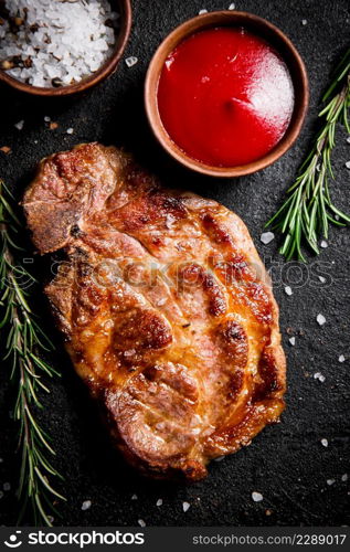 Grilled pork steak with tomato sauce and rosemary. On a black background. High quality photo. Grilled pork steak with tomato sauce and rosemary.