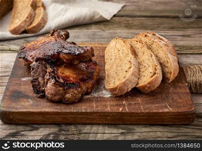 grilled pork steaks on the bone on a kitchen cutting board, baked sliced rye flour bread top view