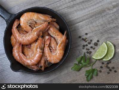 Grilled prawn shrimps in a frying pan with spices, on wooden background. Top view.