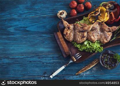Grilled quail meat with vegetable on a blue wooden background. Grilled quail meat